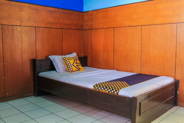 Un lit simple avec un cadre en bois et une literie blanche, placé contre un mur en bois avec un plafond bleu.