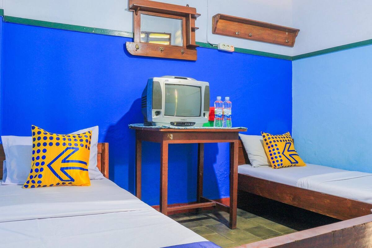 Una habitación con dos camas, una mesa de madera con un televisor y dos botellas de agua.