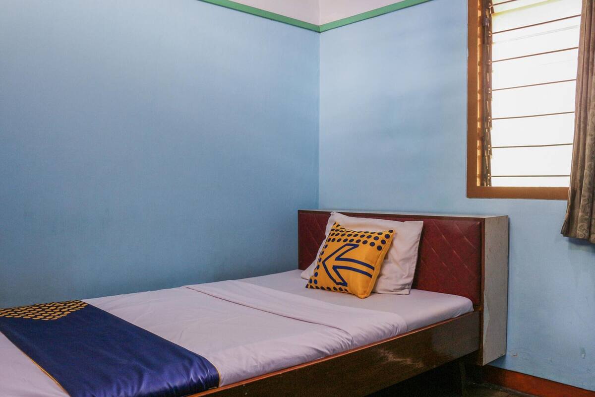 Una cama individual con cabecera, un almohadón con diseño geométrico y una manta con motivos azules y amarillos.