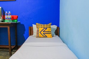 Une petite pièce étroite, avec un lit, une table de chevet en bois et un mur bleu.