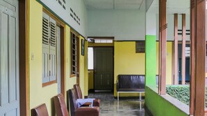 A corridor with a row of leather chairs and a bench, a door at the end, and a window with blinds.