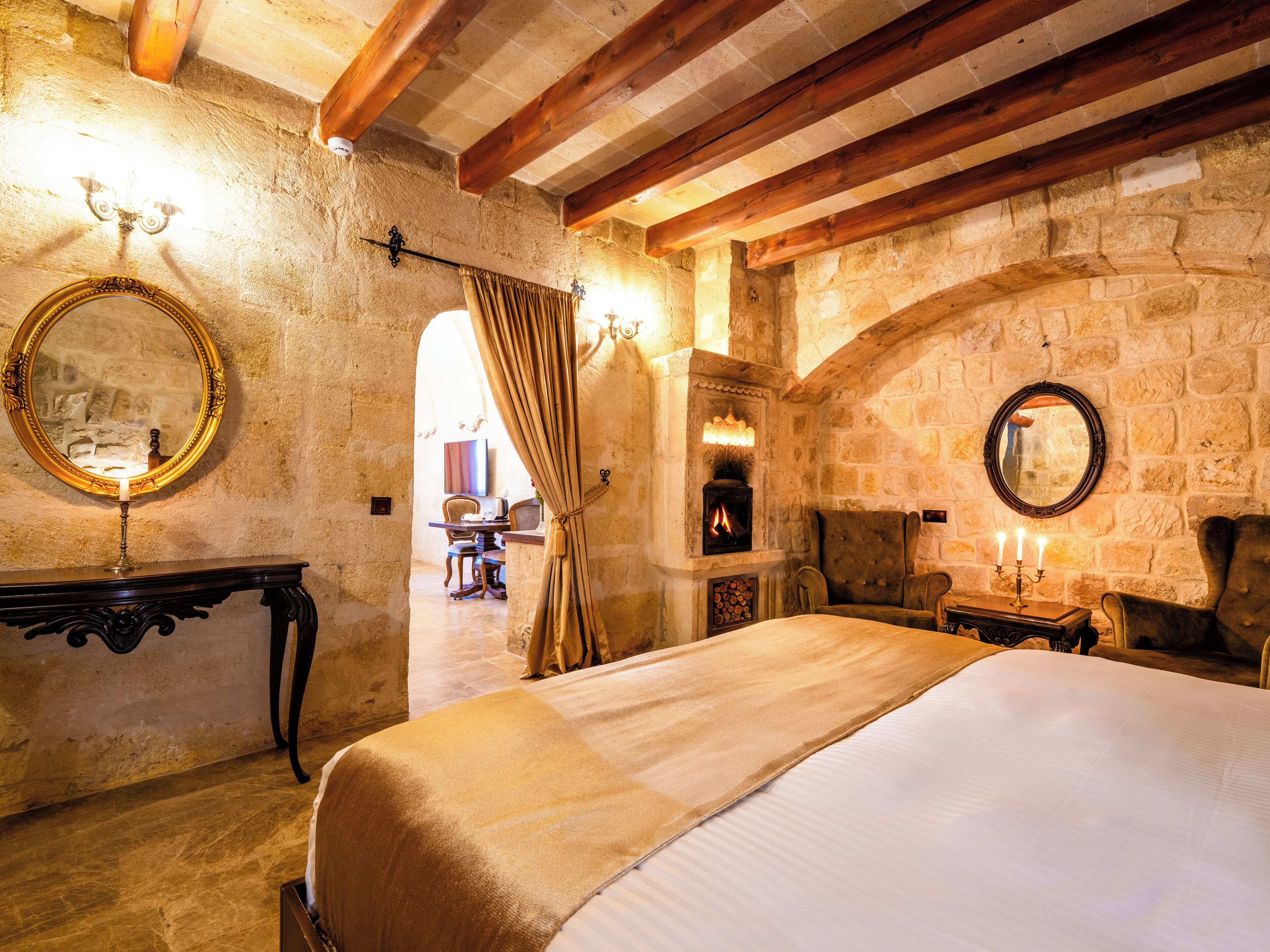 A rustic room with a stone wall, a fireplace, a bed, and a mirror.