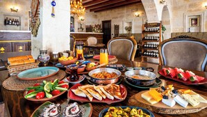 A dining area with a variety of food and drinks, wooden furniture, and a stone archway. - Zeydem Suites (Ürgüp)