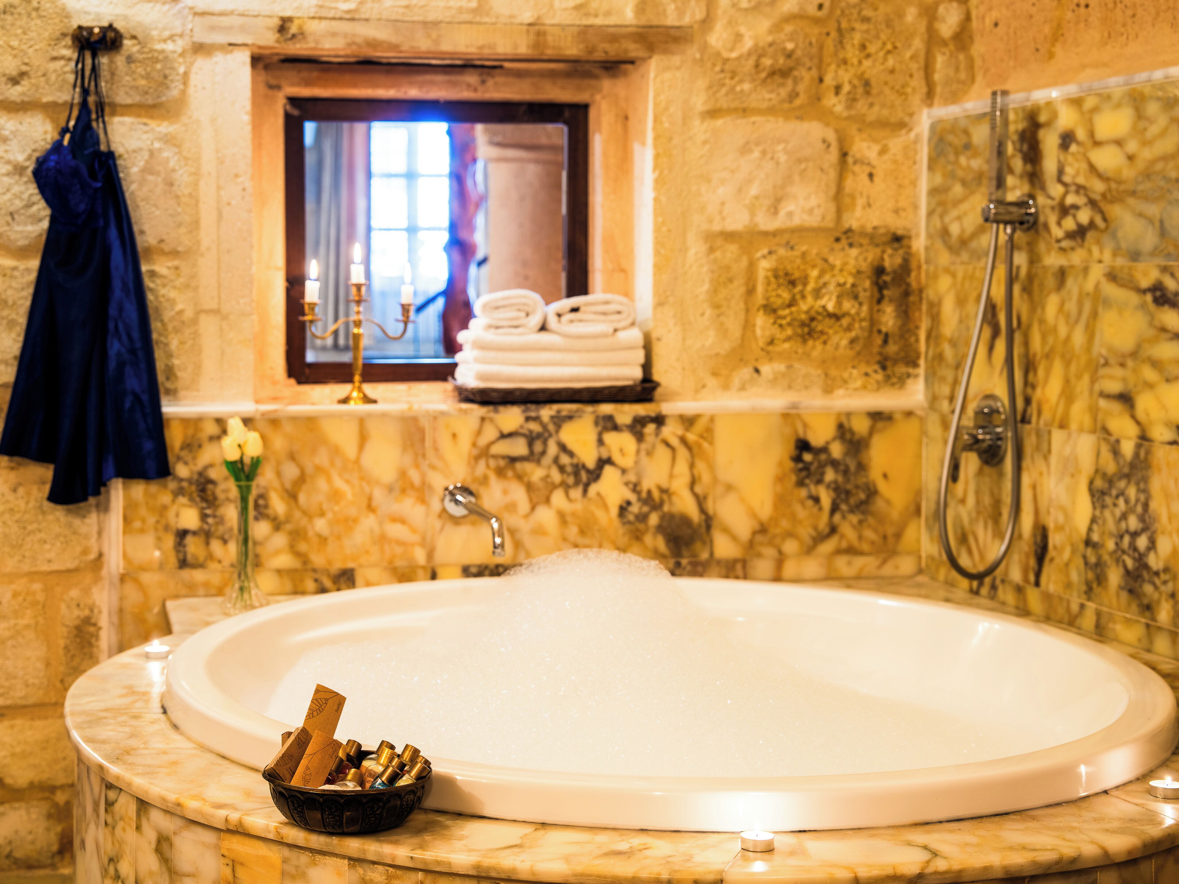 A bathroom with a marble sink, a bathtub, a shower, and a window with curtains.