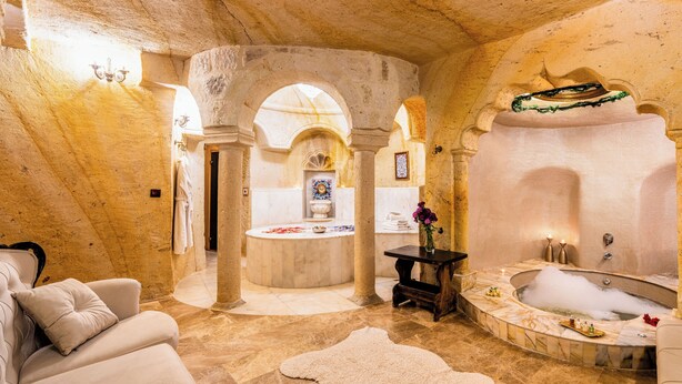 A luxurious spa room with a marble floor, a large bathtub, a sofa, and a small table with a vase. - Zeydem Suites (Ürgüp)