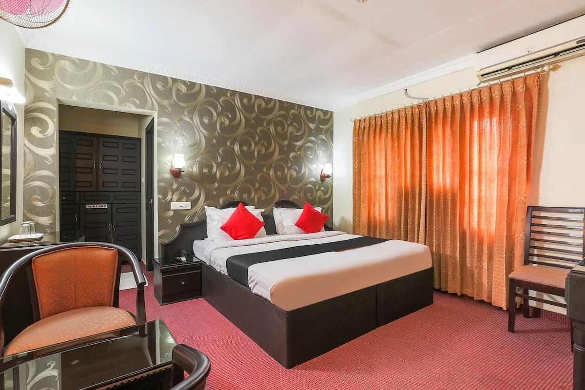 Hotellihuone, jossa on sänky, kaksi yöpöytää, tuoli, työpöytä ja peili.