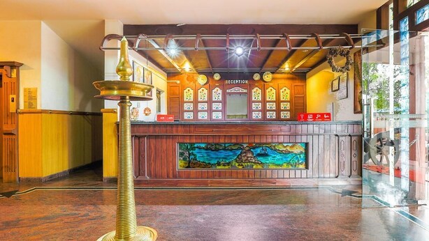 A reception area with a wooden reception desk, a large painting, and a brass lamp. - RamKripa Inn (Karwi)
