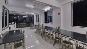 A spacious dining area with a long table and chairs, large windows, and a visible staircase. - RamKripa Inn (Karwi)