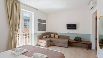 Ein Hotelzimmer mit Bett, Sofa, Sitzbank, Fernseher und einem Fenster mit Vorhängen.