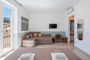 A modern bedroom with a large bed, a sofa, a TV, and a mirror.