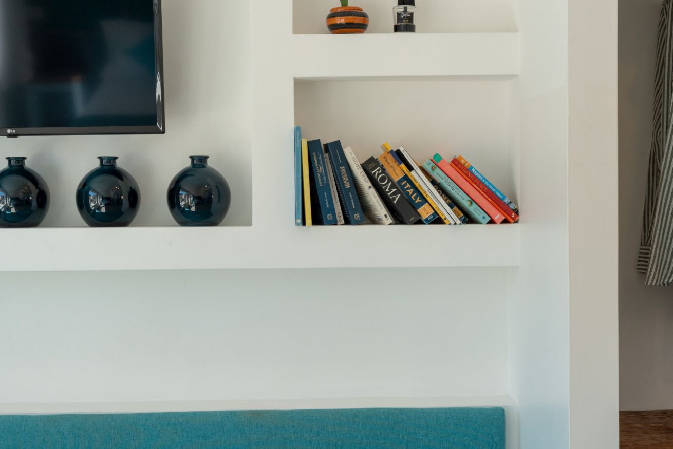 Un mur orné d’un téléviseur à écran plat, de trois vases noirs et d’une bibliothèque remplie de livres.