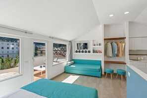 A modern bedroom with a bed, a teal sofa, a small table, and a view of the city through large windows.