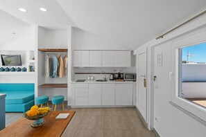 A modern kitchen with white cabinets, a sink, a kettle, and a microwave. There is a wooden dining table with a bowl of fruit. - Sorrento City View Penthouse with Terrace&Solarium (Sorrento)