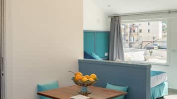 Une petite pièce moderne, avec une table en bois, un panier de fruits, des coussins de couleur turquoise et une fenêtre donnant sur des immeubles.