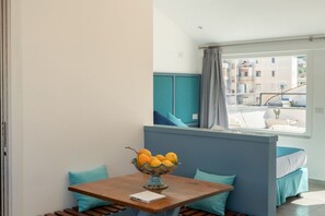 A small, modern room with a wooden table, a bowl of fruit, teal-colored cushions, and a window with a view of buildings. - Sorrento City View Penthouse with Terrace&Solarium (Sorrento)
