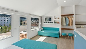 Une chambre moderne avec un lit, un canapé de couleur turquoise, une petite table et une vue sur la ville grâce à de grandes fenêtres.