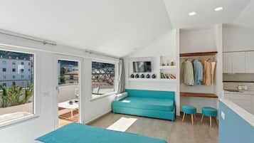 Une chambre moderne avec un lit, un canapé de couleur turquoise, une petite table et une vue sur la ville grâce à de grandes fenêtres.