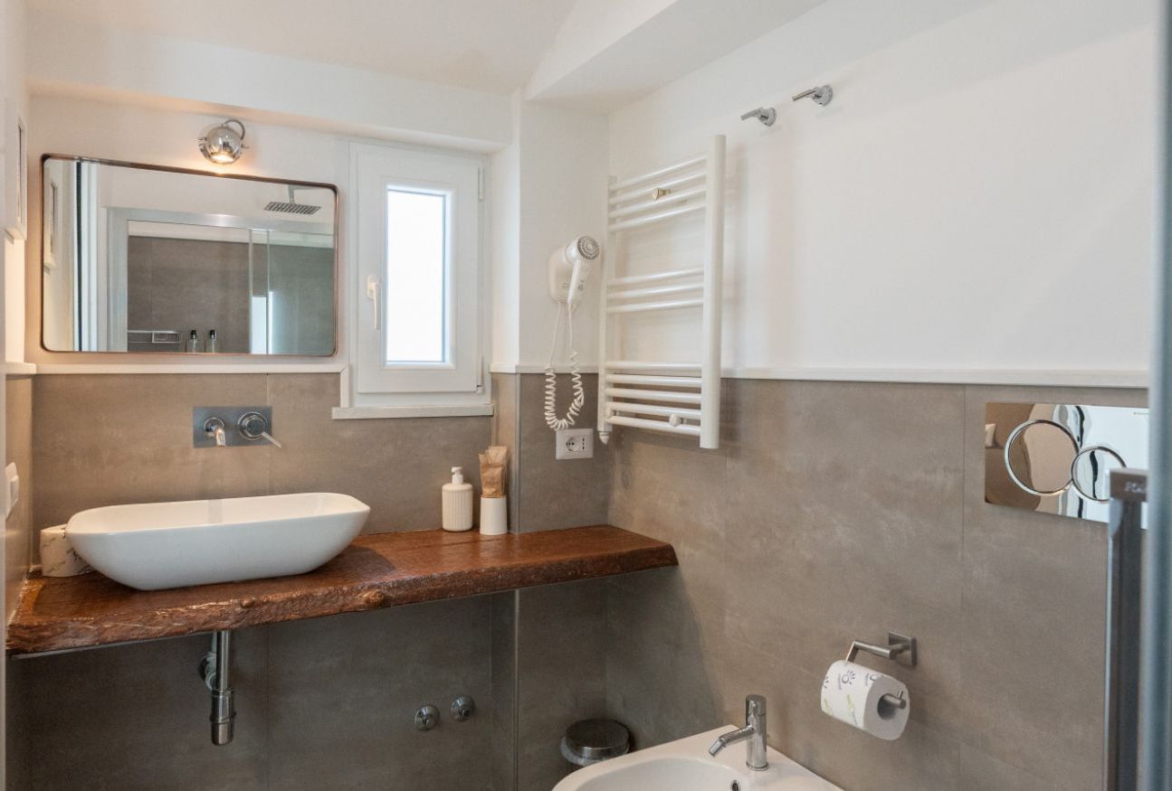 Une salle de bain moderne avec un grand miroir, un lavabo blanc, un porte-serviettes et une douchette à main.