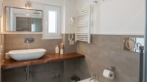 Une salle de bain moderne avec un grand miroir, un lavabo blanc, un porte-serviettes et une douchette à main.
