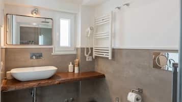 Une salle de bain moderne avec un grand miroir, un lavabo blanc, un porte-serviettes et une douchette à main.