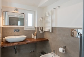 A modern bathroom with a large mirror, a white sink, a towel rack, and a handheld showerhead.