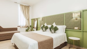 Habitación de hotel con una cama grande, un sofá pequeño, una mesita de noche y una ventana con cortinas.