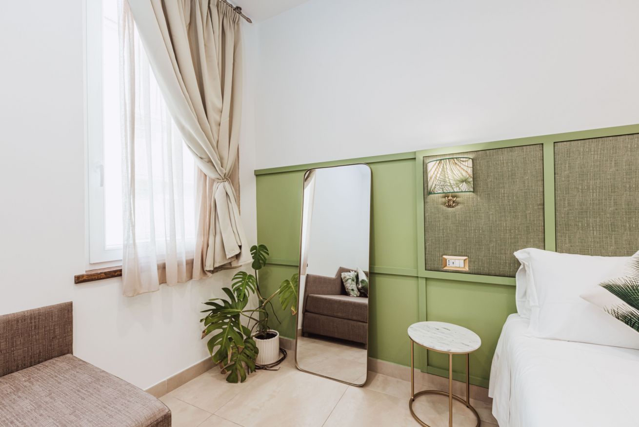 Una habitación moderna con una pared verde decorativa, un espejo grande, una mesita redonda pequeña, un sofá y una planta en maceta.