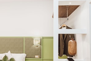 Un dormitorio con cabecera verde, una lámpara colgante y un perchero con un jarrón.
