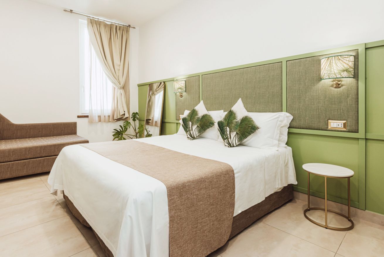 Ein Hotelzimmer mit einem großen Bett, einem kleinen Sofa, einem Nachttisch und einem Fenster mit Vorhängen.