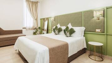 Ein Hotelzimmer mit einem großen Bett, einem kleinen Sofa, einem Nachttisch und einem Fenster mit Vorhängen.