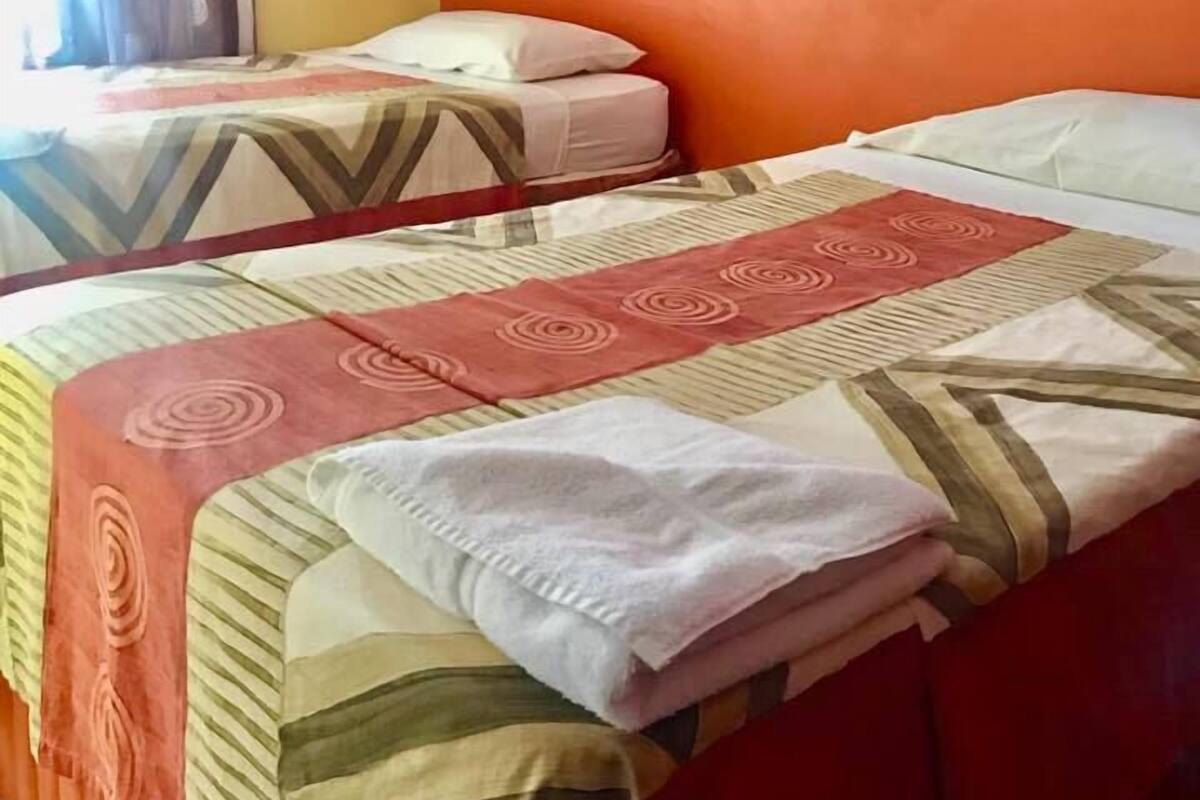Ein Zimmer mit zwei Betten, beide mit gemusterten Bettwaren und Kissen. An der Wand h ängen zwei gerahmte Bilder.