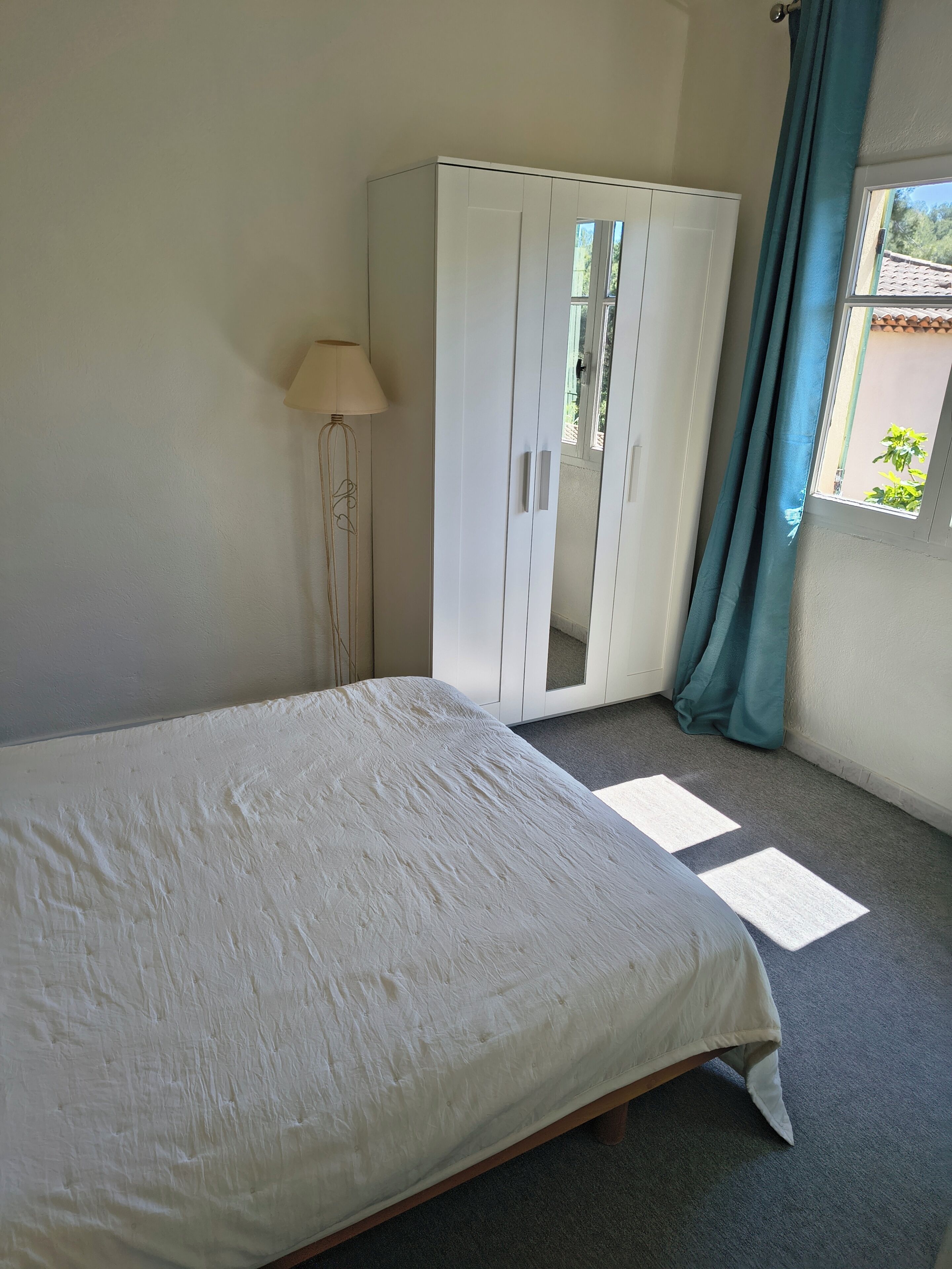 A bedroom with a bed, a wardrobe, a floor lamp, and a window with curtains.