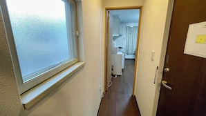 A narrow hallway with a window on the left, leading to a kitchen area with cabinets and appliances. - Happy Osaka House (Osaka)