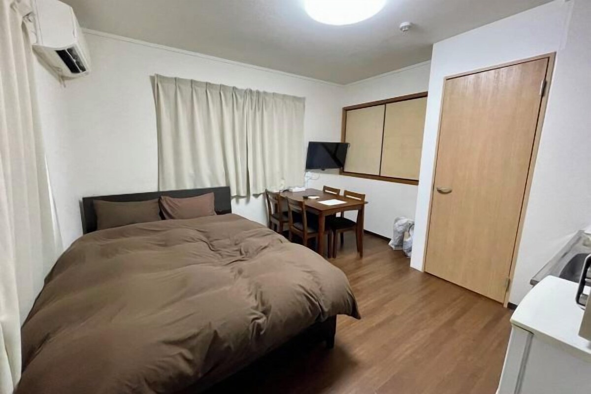 A hotel room with a bed, a desk, a chair, a television, and a wardrobe.