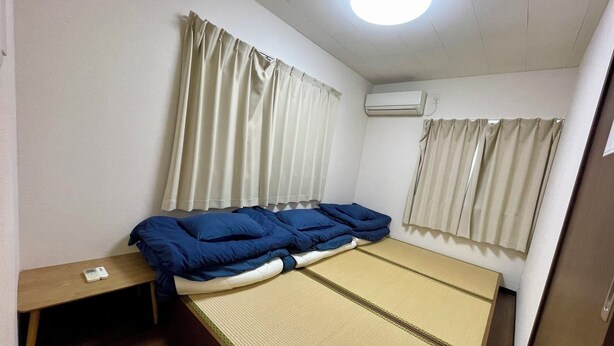 A room with a bed, a small table, and an air conditioning unit. - Happy Osaka House (Osaka)