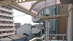 A narrow corridor with a metal railing, a concrete floor, and a view of buildings in the background. - Happy Osaka House (Osaka)
