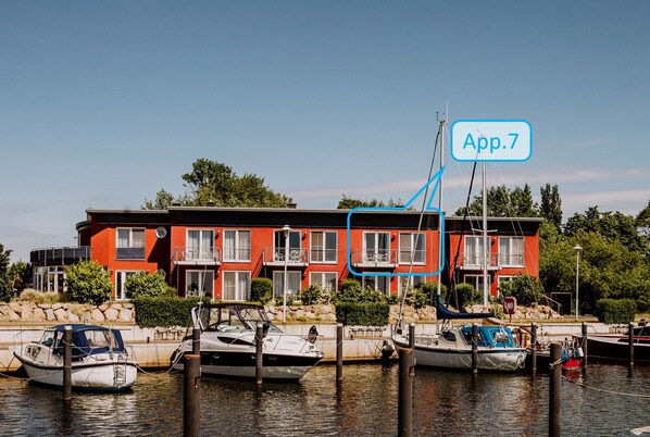 A waterfront property with a red building, multiple balconies, and boats docked in the water.