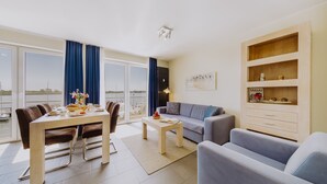 A modern living room with a dining area, a sofa, a coffee table, and a bookshelf. - Apartment in the harbor (Puddemin)