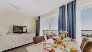 A dining area with a table set for breakfast, a television, and a view of the water. - Apartment in the harbor (Puddemin)