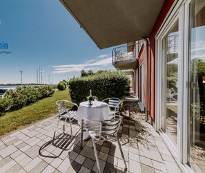 A patio with a table and chairs, a bottle of champagne, and a view of the water and boats.