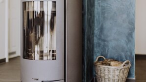 A modern, cylindrical wood stove with a glass door, positioned against a textured wall. - Apartment in the harbor (Puddemin)