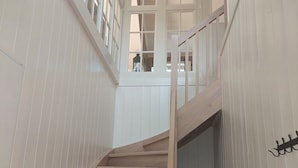Eine Holztreppe mit weiß getäfelten Wänden, die zu einer Empfangshalle mit großen Fenstern führt.
