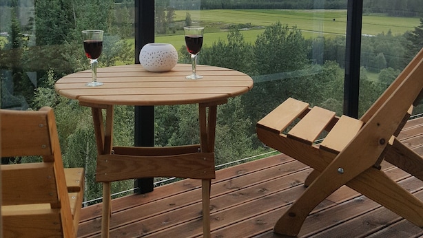 Ein Holztisch mit zwei Weingläsern und einem weißen Dekorationsobjekt auf einem Balkon mit Blick auf eine Berglandschaft.