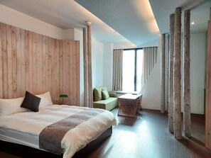 A modern hotel room with a large bed, a small sofa, a dining table, and a view of the outdoors through large windows. - San Jo Hostel (Kaohsiung)