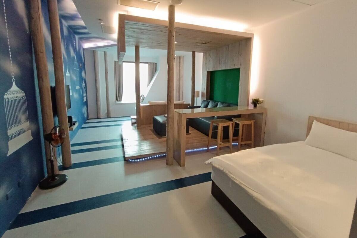 A hotel room with a bed, a desk, and a seating area. There is a large window and a view of the outside.