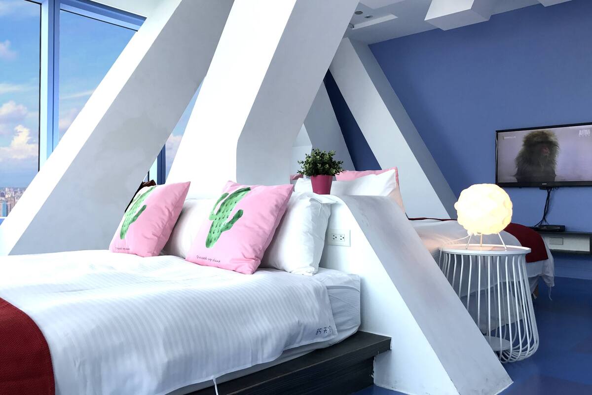 A modern bedroom with a bed, pillows, a small table, a plant, and a TV.