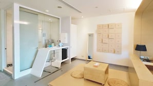 Un baño moderno con cabina de ducha de vidrio, un tocador blanco con espejo y un banco de madera con esteras tejidas.