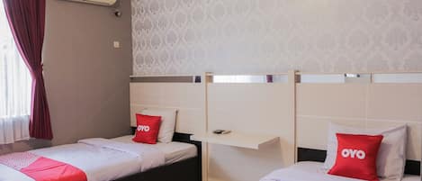 A hotel room with two beds, each with a red OYO pillow, a white headboard, and a small shelf.