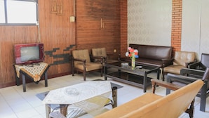 A living room with a wooden wall, a brown leather sofa, a glass coffee table, and a TV on a wooden stand.