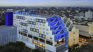 Ein modernes Hotel mit einem gut sichtbaren 'NOVOTEL SUITES' Schild, das eine markante, blaue Glasfassade und mehrere Balkone aufweist.